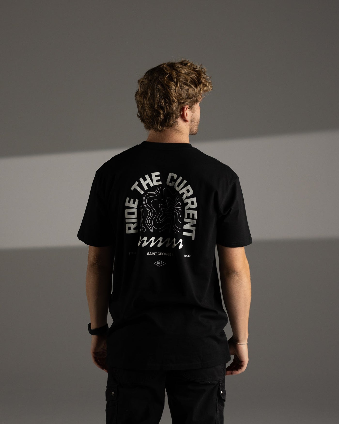 Man wearing a black t-shirt with text on the back against a gray background