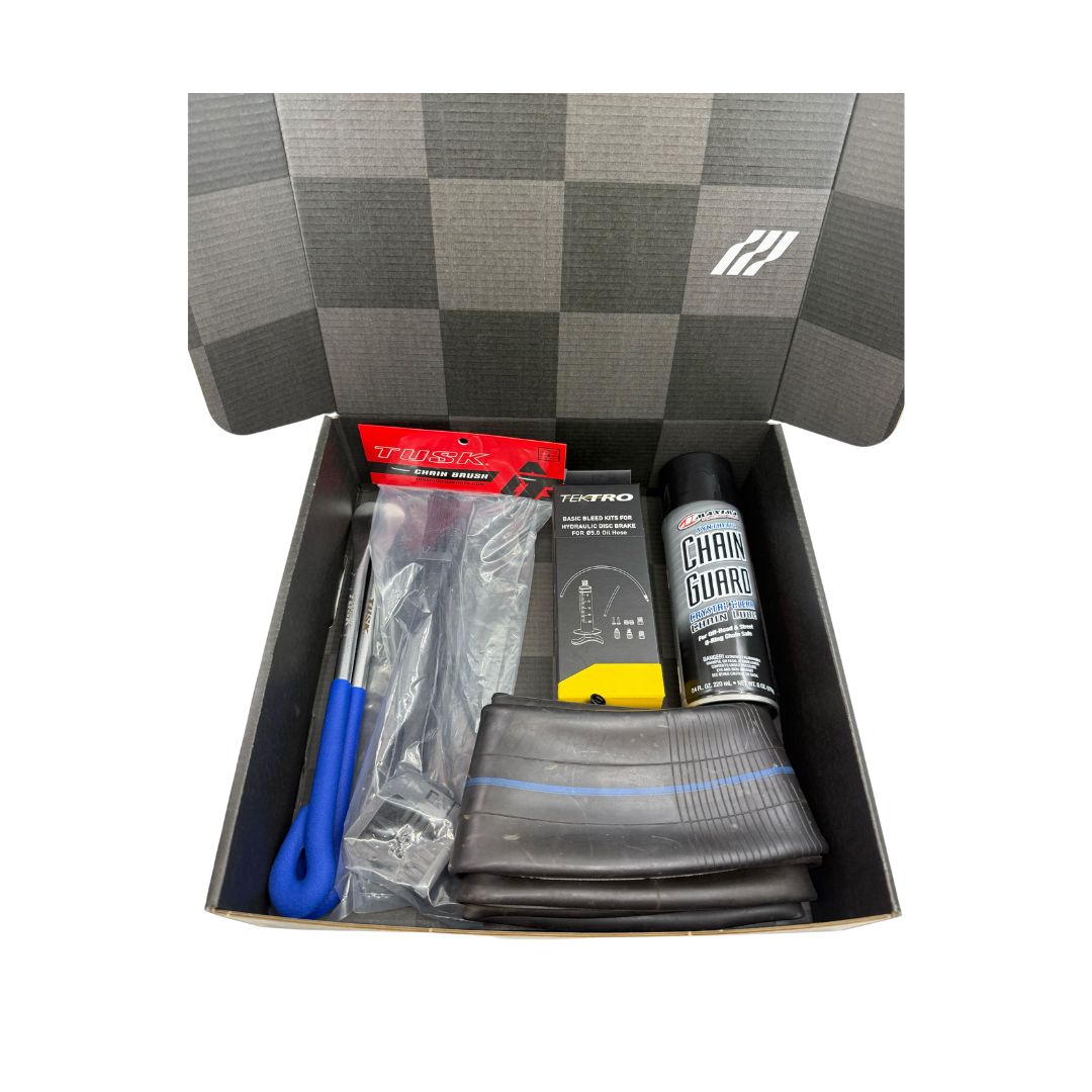 Open the Essential E-Moto Care Kit by Amped Bikes, featuring a checkered lid design and essential bicycle maintenance items: chain lubricant spray, tire lever tool, inner tube, brake pads, and a repair kit to keep your ride smooth and safe.