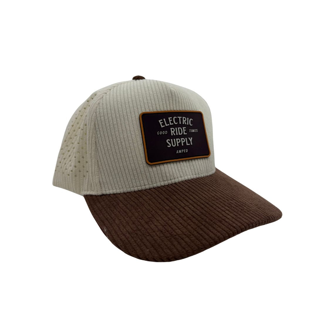 A corduroy trucker cap with a light beige front panel and a dark brown curved brim, featuring a dark brown rectangular patch on the front with the text 'ELECTRIC Ride SUPPLY'.