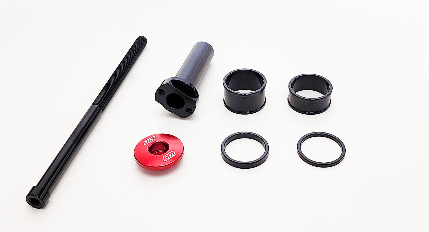 Warp9s Stem Lock automotive parts are set against a white background, showcasing a long black bolt, cylindrical black spacer, red cap with STI text, three black cylindrical rings, and two O-rings. Perfect for use with components like steering tubes or triple clamps.