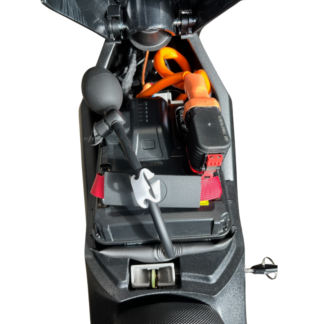 Top view of an electric scooter’s open compartment showing the battery, an orange charging cable, and the Amped Bikes Air Wedge Bag Pump Leveling and Alignment Tool neatly stored with other accessories.
