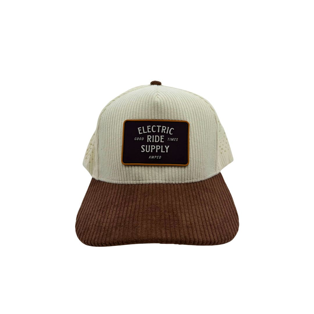 A two-tone corduroy snapback with an off-white front panel and brown brim, and a mesh back. It features a rectangular black patch on the front with the text 'ELECTRIC GOOD RIDE TIMES SUPPLY' and 'Amped' below it.