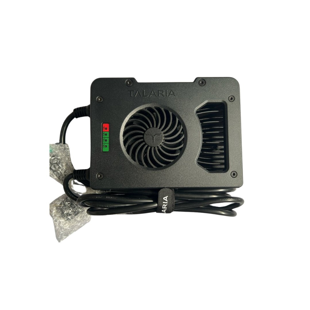 The Talaria Charger is a black electronic device resembling the Talaria OEM Battery Charger. It includes a fan, wiring, and a control panel with red and green indicators. Partially wrapped in bubble wrap, this 12 amp charger by Talaria is designed for efficiency.