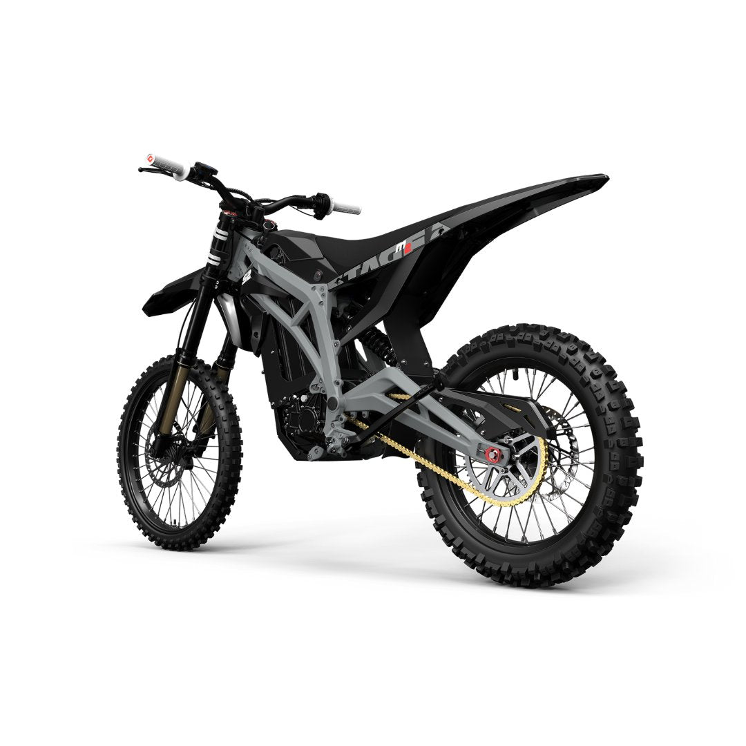 The Razor Stage2 M2 72V Electric Dirt Bike features a black and gray design, reaches 65 MPH, and is equipped with knobby tires, a robust frame, and minimalist seat. A gold chain and reinforced suspension enhance its rugged build for off-road use. It includes a swappable lithium battery for convenience.