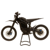 A sleek Talaria Sting MX5 Pro electric dirt bike is on a stand, viewed side-on. It boasts knobby tires, a streamlined seat, sturdy frame, and reflective surfaces. Powered by a 72V/40Ah battery, it has no visible branding or decals and sports a black finish.