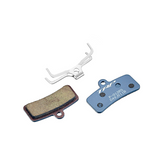 The Amped Bikes TRP P-Q12RS Disc Brake Pads set includes two pads and a silver S-shaped spring. One pad is greenish-brown with a worn surface; the other is blue with white text, compatible with 4-piston calipers.